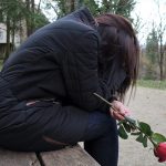 sad girl on bench holding a rose