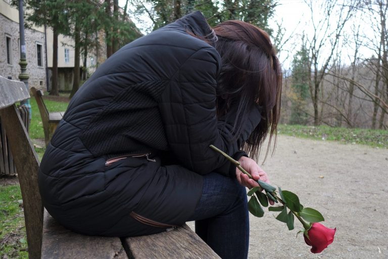 sad girl on bench holding a rose